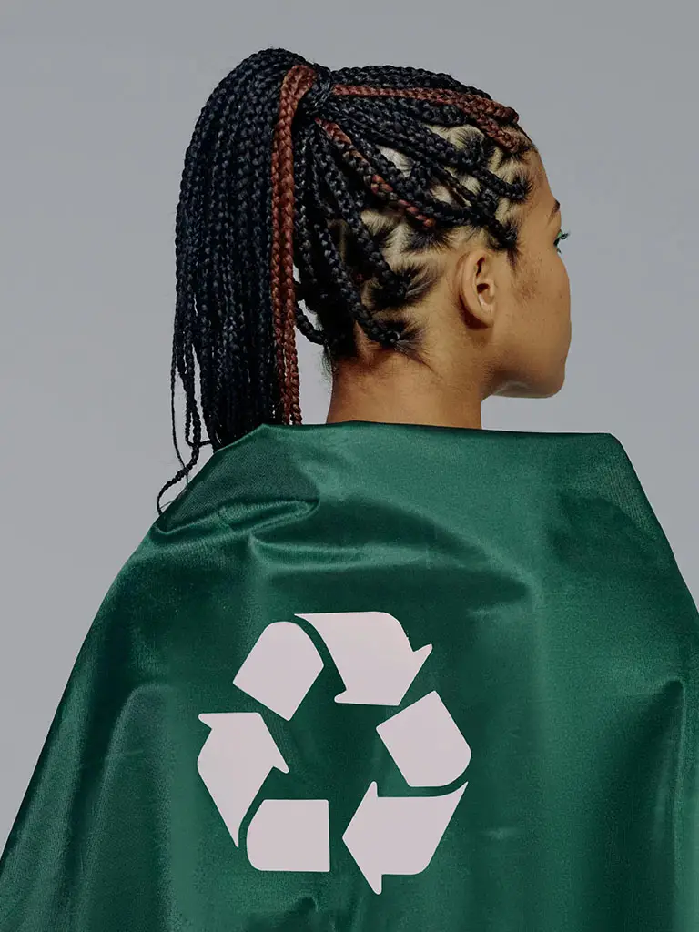 Girl wearing a green plastic cape with a recycle symbol on her back.