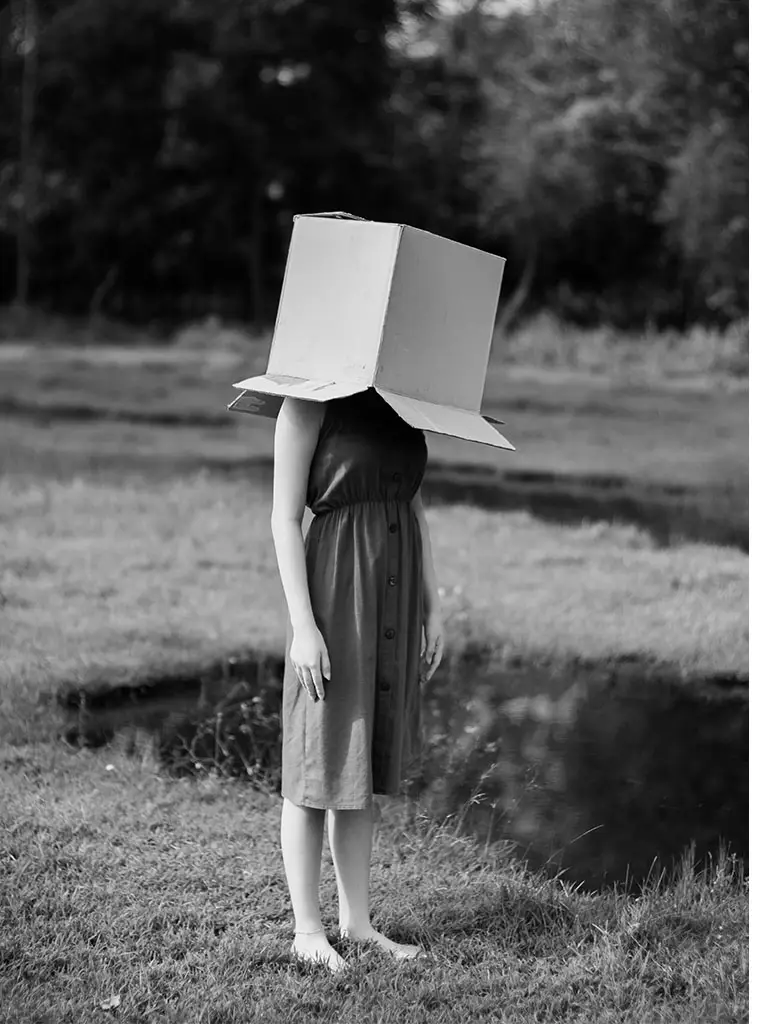 Girl standing barefoot with a cardboard box on her head representing a denial of climate change, a classic feature of climate psychology.