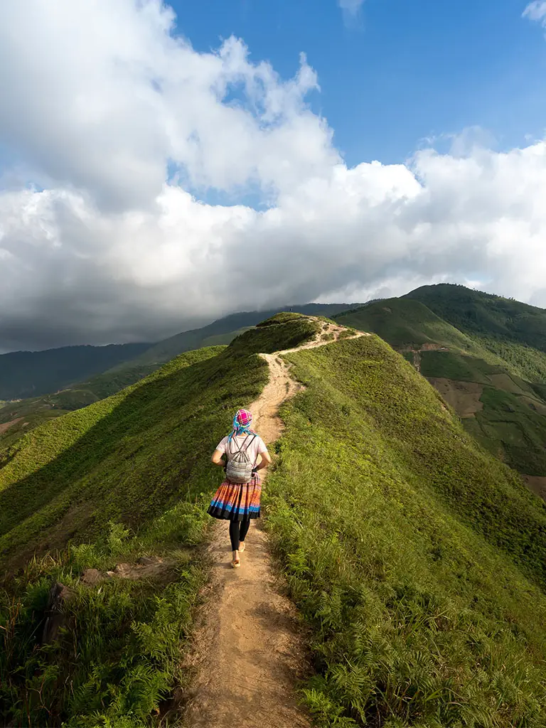 Hiker walking along footpath on a pretty ridge. Clouds in the background. SHows the idea of sustainable travel.