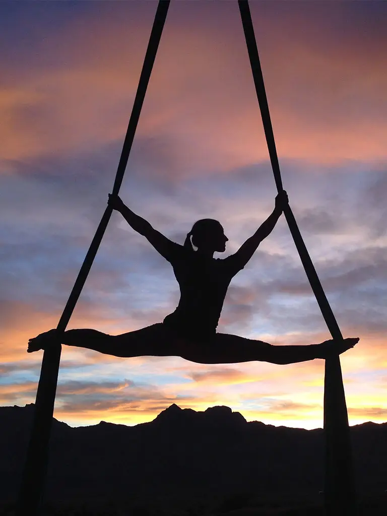 Girl doing yoga and gymnastics between two ropes at sunset doing the splits showing a sustainable way to practice sports.