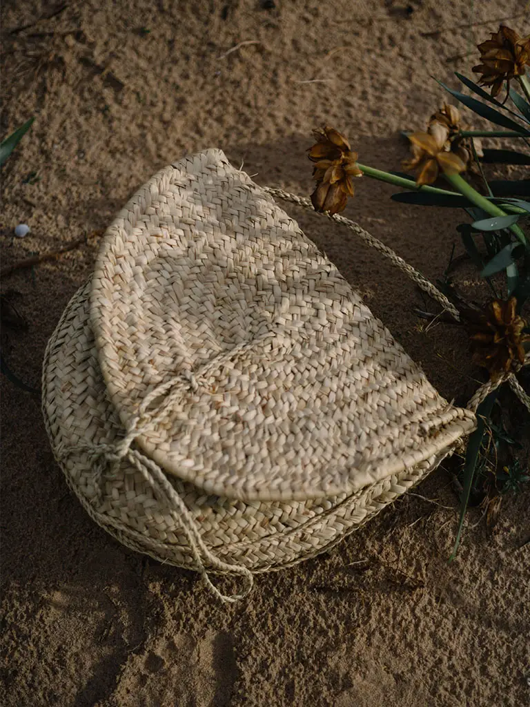 Sustainable accessories which here are a natural wicker handbag on sand