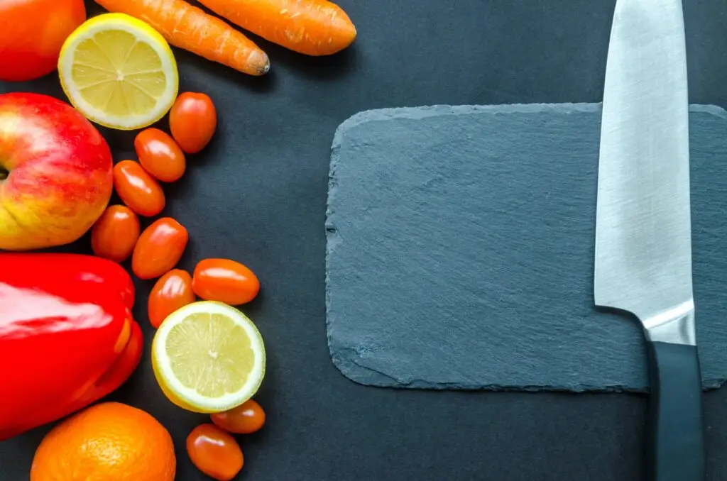 Carrots, lemons and tomatoes next to a slate chopping board to show vegetarian sustainable food choices.