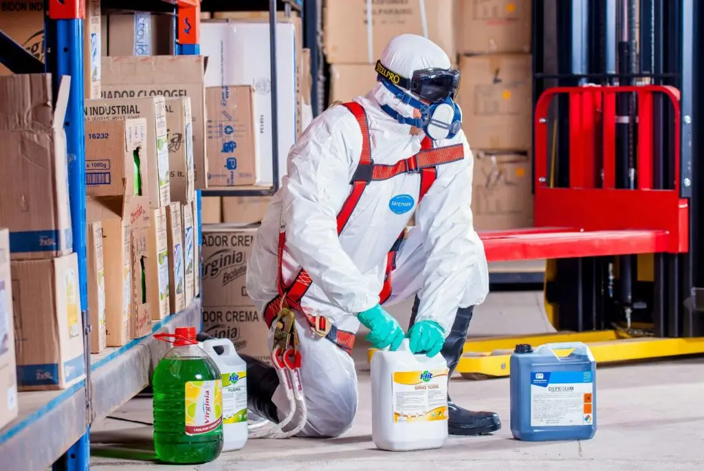 Person dress in white suit and googles to protect them from the containers of chemicals they are holding.  Showing the impact of chemicals on the ecosystem.