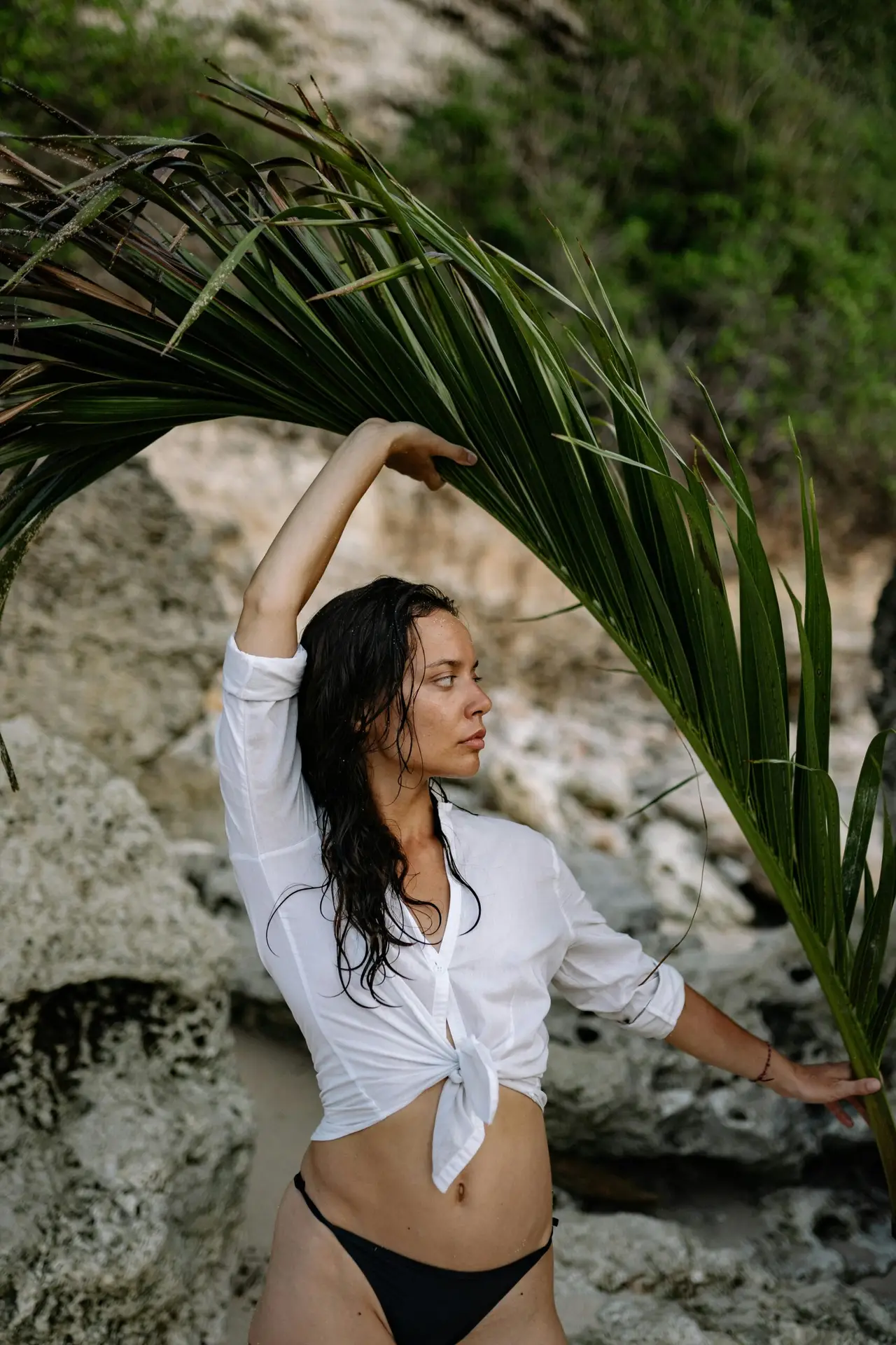 Female wearing a white shirt and bikini bottoms holding a large palm leaf in nature to symbolise eco-friendly fashion