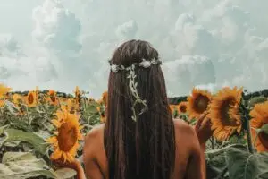 Girl with long dark hair and head braid walking through field of sunflowers. Can only see the girl from behind.